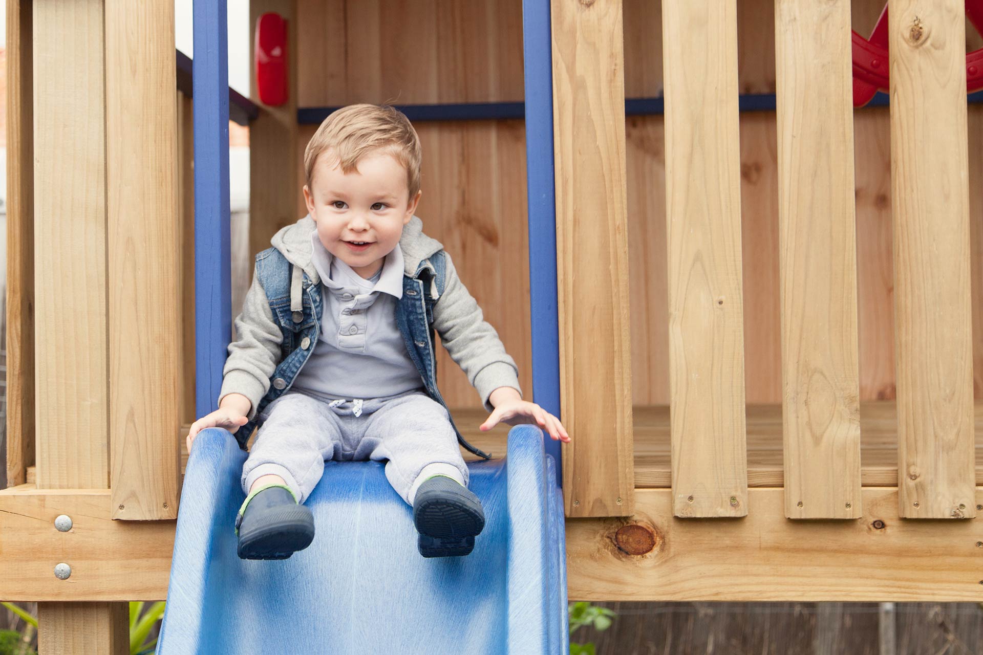Kleinkind sitzt auf einer blauen Rutsche eines Holzspielturms